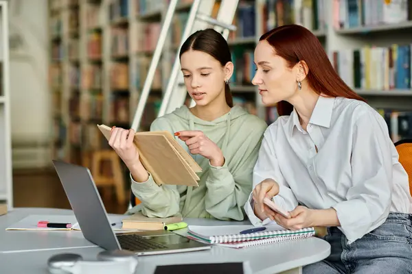 Un tutor rossa insegna una ragazza adolescente in una biblioteca, entrambi assorbiti in un computer portatile per le lezioni post-scuola. — Foto stock