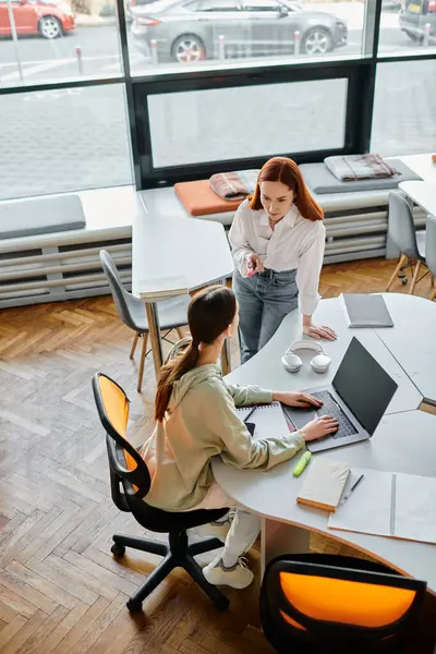 Redhead tutor teaching teenage girl in an office setting, both focused on laptop work for modern education. — Stock Photo