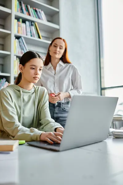 A tutor with red hair and a teenage student, sit at a desk, focused on their laptop during after school lessons. — Stock Photo