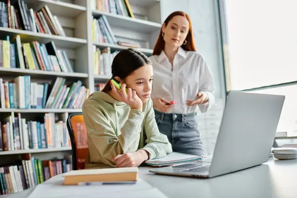A focused tutor, a redheaded woman, talks on the phone while sitting at a desk with a laptop during an after-school lesson. — Stock Photo