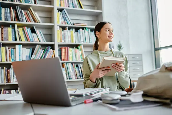 Ein Teenager sitzt an einem Schreibtisch mit Laptop, umgeben von Bücherregalen, und konzentriert sich auf die Hausaufgaben nach der Schule.. — Stockfoto