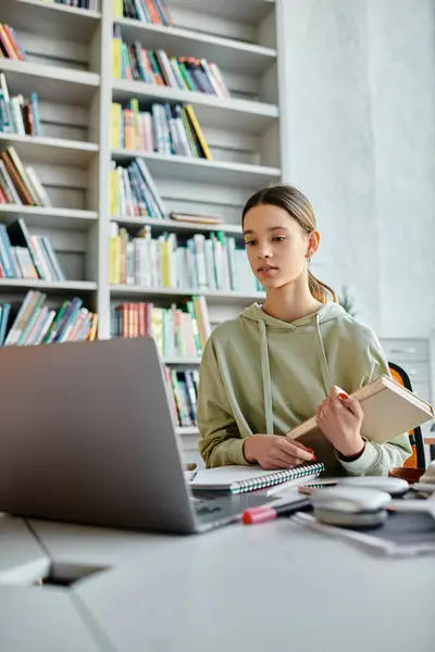 A teenager engrossed in modern education, surrounded by books and a laptop, diligently doing homework at a desk. — Stock Photo