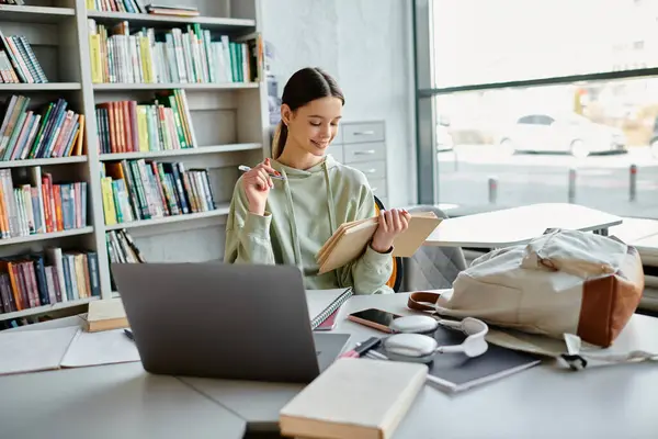 A teenage girl engrossed in homework on a laptop, seated at a desk next to a bookshelf. — Stock Photo