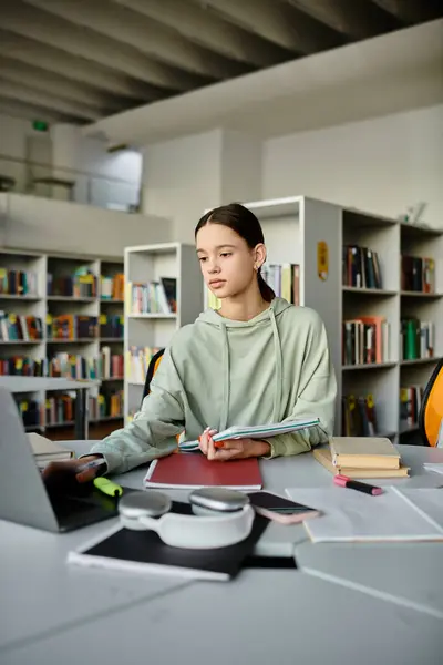 A teenage girl sits at a desk in a library, focusing intently on her laptop while doing homework after school. — Stock Photo