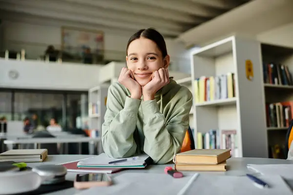 Una adolescente, después de la escuela, se sienta en un escritorio de la biblioteca, absorta en su tarea en un ordenador portátil en un ambiente tranquilo y sereno. - foto de stock