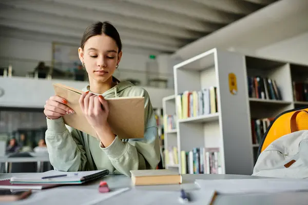 Ein Mädchen im Teenager-Alter sitzt an einem Schreibtisch und schreibt fleißig in ein Notizbuch, konzentriert auf ihre Schularbeiten nach Stunden des Lernens. — Stockfoto