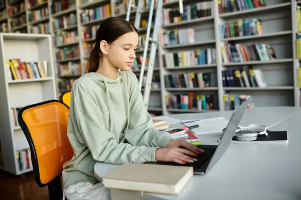 Un'adolescente che studia diligentemente alla scrivania con un computer portatile, circondata da scaffali pieni di libri. — Foto stock