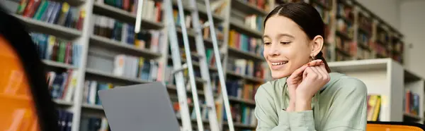 A young woman immersed in her laptop, surrounded by books in a quiet library setting. — Stock Photo