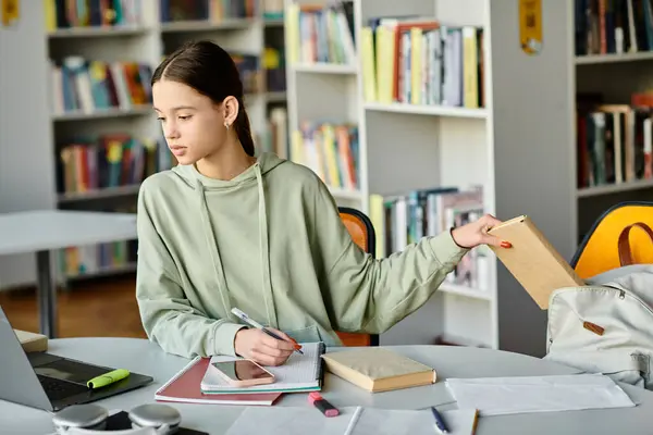 A teenage girl immersed in modern education, homework on laptop in a library, surrounded by books. — Stock Photo