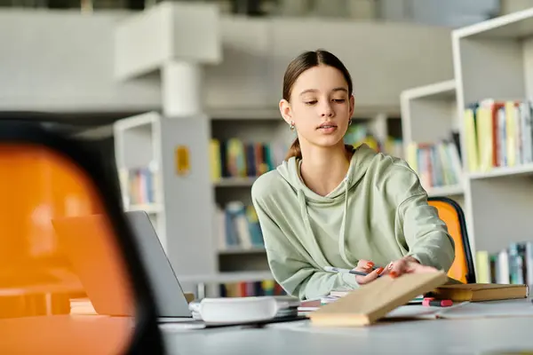 A teenage girl sits at a library table, absorbed in her schoolwork on a laptop, surrounded by books and the peaceful atmosphere of the library. — Stock Photo