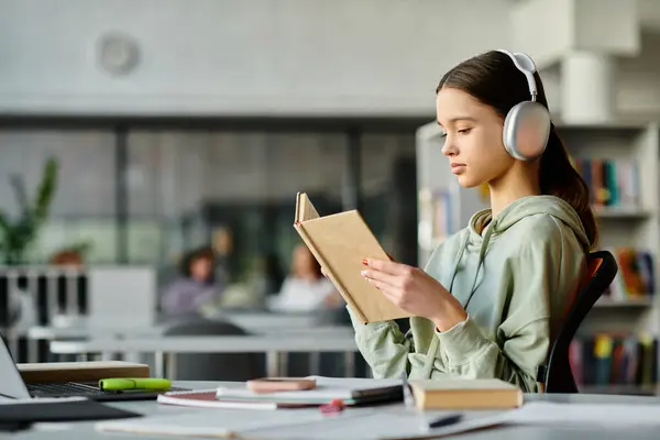 A teenage girl engrossed in a library book while wearing headphones, immersing herself in the realms of literature and music. — Stock Photo