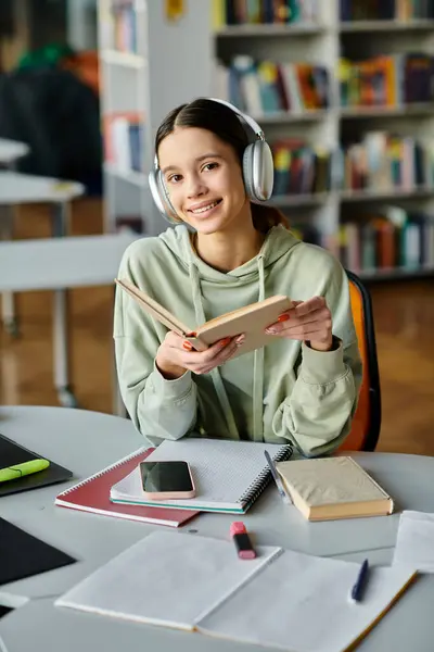 A teenage girl engrossed in a book with headphones on, immersed in peaceful solitude in a library. — Stock Photo