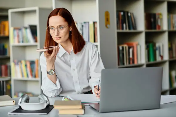Una tutor rossa si siede ad una scrivania, concentrata sull'insegnamento di una lezione online con un computer portatile, dopo la scuola. — Foto stock