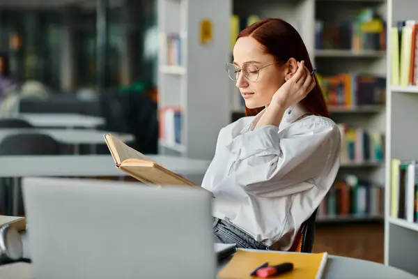 Una donna dai capelli rossi immersa in un libro in una serena biblioteca, assorbita nella lettura e nell'apprendimento. — Foto stock