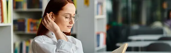 Una donna dai capelli rossi avvolta in un libro, circondata da scaffali in una biblioteca, immersa nell'atto di leggere. — Foto stock