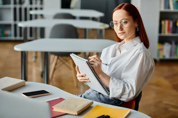 Una rossa concentrata, un tutor, seduta a una scrivania, che scrive sugli appunti durante una lezione del doposcuola.. — Foto stock