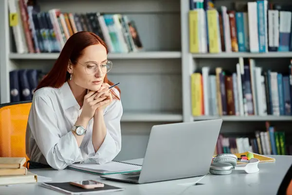Un tutor donna dai capelli rossi sta insegnando una lezione online utilizzando un computer portatile presso una scrivania. — Foto stock