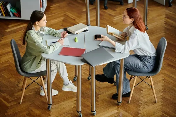 Redhead donna tutor una ragazza adolescente a un tavolo in un ufficio moderno, utilizzando un computer portatile per lezioni post-scuola. — Foto stock