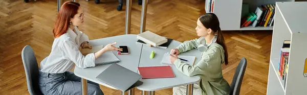 Руда жінка навчає дівчину-підлітка за столом в офісі, використовуючи ноутбук для уроків після школи. — стокове фото