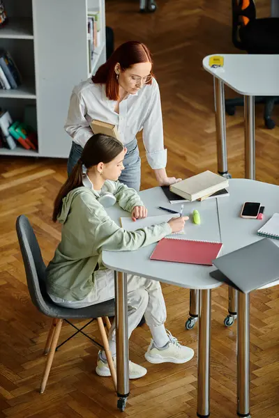 Eine rothaarige Frau unterrichtet ein Mädchen im Teenageralter in einem Klassenzimmer, beide nehmen mit einem Laptop an einer Nachmittagsstunde teil.. — Stockfoto