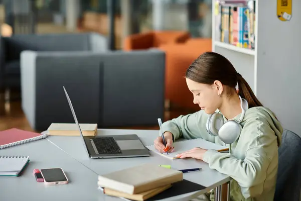 Дівчина-підліток за столом, загорнута в ноутбук під час виконання домашнього завдання — стокове фото