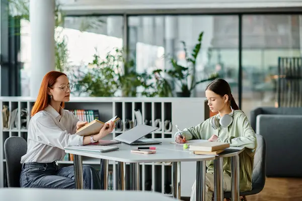 Una rossa insegna a un'adolescente in un ufficio, entrambe impegnate in lezioni post-scolastiche usando un computer portatile per l'educazione moderna.. — Foto stock