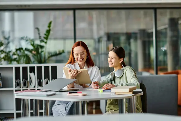 Une rousse donne des cours particuliers à une adolescente à une table dans un bureau, en utilisant un ordinateur portable pour l'éducation moderne après les cours d'école. — Photo de stock