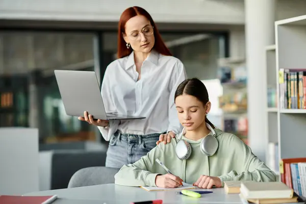 Una donna dai capelli rossi istruisce un'adolescente a una scrivania con un computer portatile, impegnata in lezioni post-scolastiche.. — Foto stock