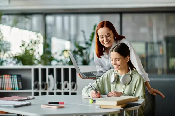 Una rossa insegna a un'adolescente alla scrivania, entrambe concentrate su un computer portatile durante una sessione di tutoraggio dopo la scuola.. — Foto stock