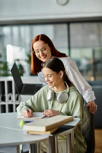 Eine rothaarige Frau unterrichtet ein Teenager-Mädchen an einem Tisch in einem Büro, beide konzentrieren sich nach dem Unterricht auf einen Laptop.. — Stockfoto