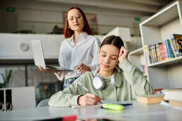 Un tuteur - une rousse - enseigne à une adolescente à un bureau à l'aide d'un ordinateur portable pour les leçons après l'école. — Photo de stock