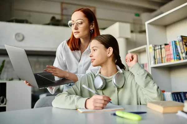 Redhead woman tutors teenage girl in library, both engrossed in laptop for modern after-school lessons. — Stock Photo