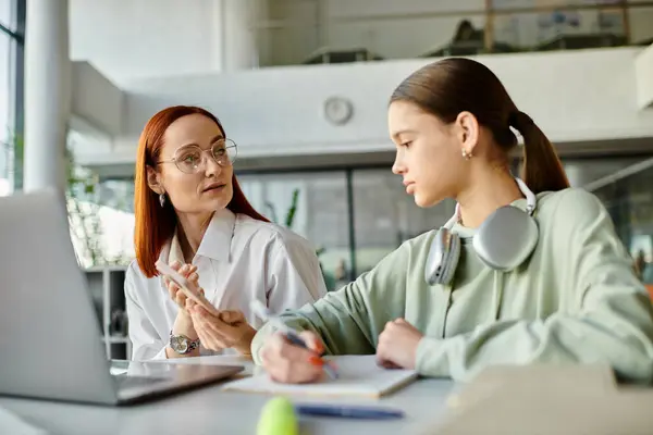 Una donna rossa tutor una ragazza adolescente a una scrivania, impegnata in una conversazione durante l'utilizzo di un computer portatile per l'educazione moderna. — Foto stock