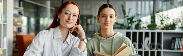 Rossa tutor donna adolescente in biblioteca, entrambi assorti nel libro — Foto stock