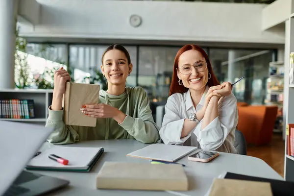 Una donna rossa tutor una ragazza adolescente a un tavolo in un ufficio, impegnato in lezioni post-scuola utilizzando un computer portatile. — Foto stock