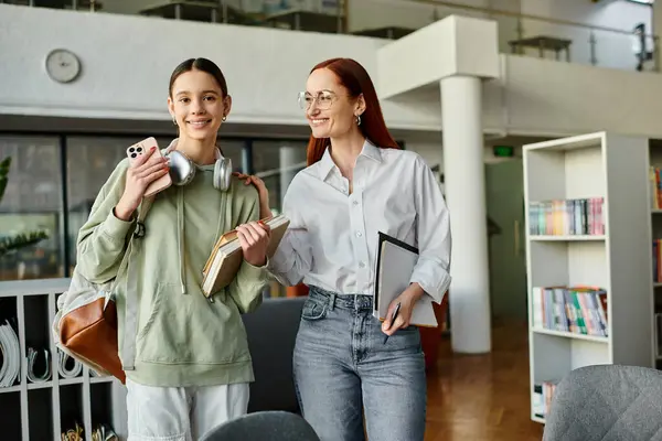 Una rossa fa da tutor a un'adolescente in una biblioteca, entrambe con dei libri, assorte nelle lezioni del doposcuola. — Foto stock