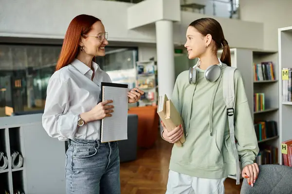 A redhead woman tutors a teenage girl in a library, engaging in after-school lessons — Stock Photo