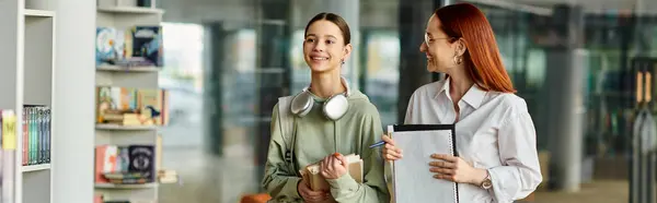 Redhead woman teaching a teenage girl in a modern library setting, engaging in after school lessons. — Stock Photo