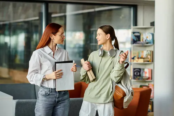 A redhead woman guides a teenage girl through studies in a modern library. — Stock Photo