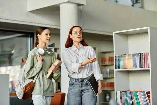 A redhead woman teaches a teenage girl in a library, engrossed in books — Stock Photo