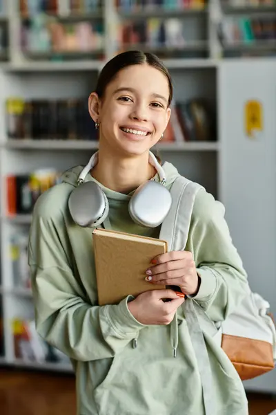 Un'adolescente ascolta un audiolibro con le cuffie mentre tiene un libro in una biblioteca. — Foto stock