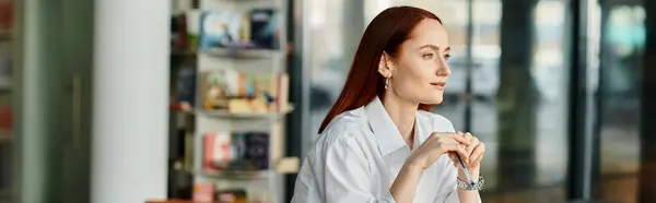 A redheaded woman in a white shirt sits at a table, a modern educational setting. — Stock Photo