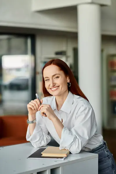 A redheaded woman sitting at a desk with a pen in hand, tutoring at after-school lessons. — Stock Photo