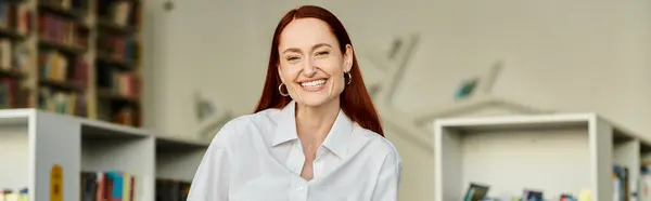 A redheaded woman smiles after tutoring in a library, after-school lessons. — Stock Photo