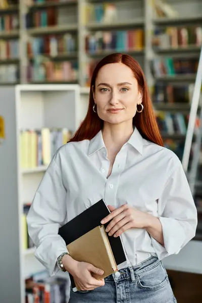 In a library, a redhead woman holds a book, after-school lessons. — Stock Photo