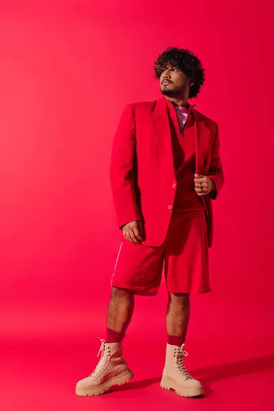 Um jovem indiano dapper em um terno vermelho impressionante e gravata marcando uma pose contra um fundo vermelho vívido. — Fotografia de Stock