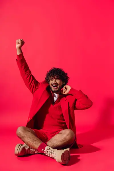 A handsome young Indian man sitting on the ground with his arms raised in the air. — Stock Photo