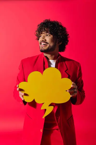 Um jovem indiano elegante em um terno vermelho segurando uma bolha de fala amarela brilhante. — Fotografia de Stock