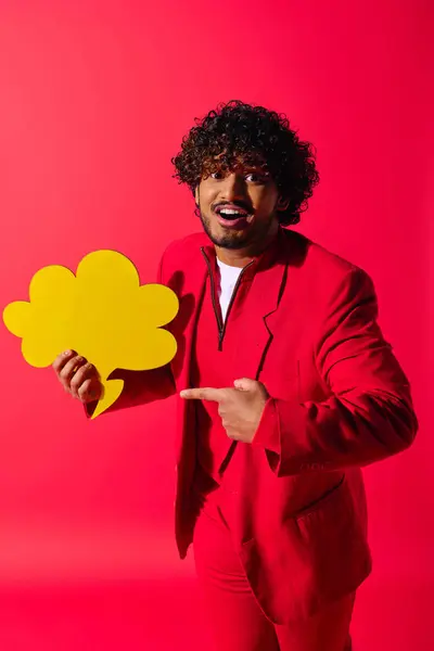 Schöner junger indischer Mann im roten Anzug mit einer gelben Sprechblase vor lebendigem Hintergrund. — Stockfoto