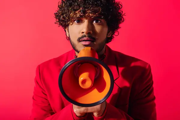 Schöner junger indischer Mann mit lockigem Haar hält rotes und schwarzes Megafon in der Hand. — Stockfoto